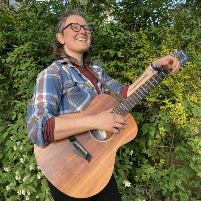 kimberley Moore with guitar outside green border in the garden